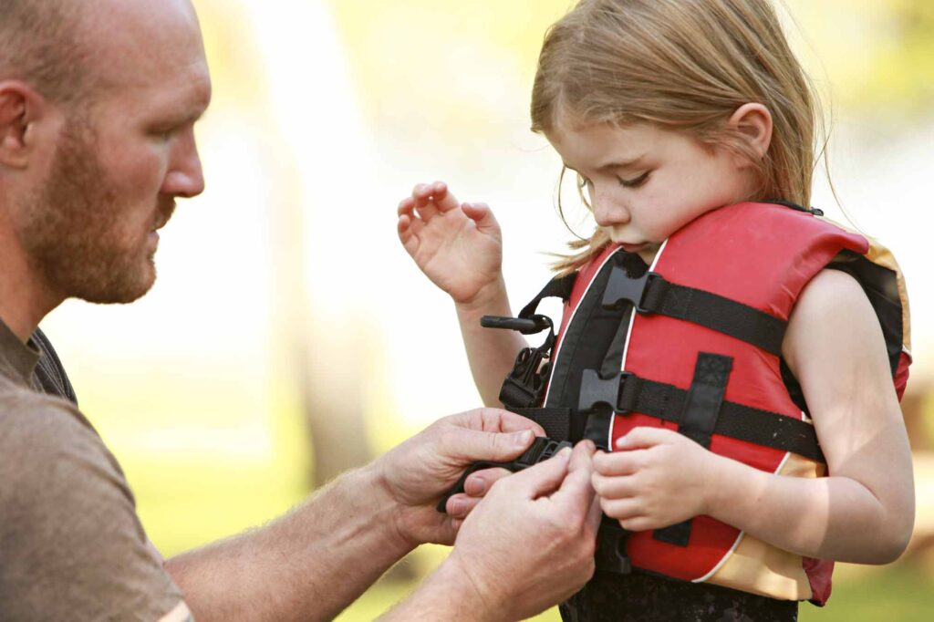 father fastening daughter's life jacket